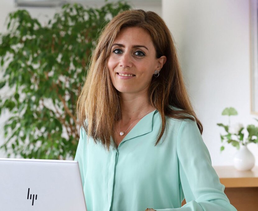 Laura Schneider sitzt am Laptop und lacht in die Kamera | © ask! – Beratungsdienste für Ausbildung und Beruf