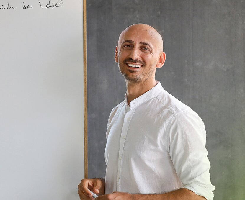 Özkan Ünlü vor einem Whiteboard mit einem Stift in der Hand in einer Beratung | © ask! – Beratungsdienste für Ausbildung und Beruf
