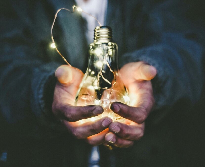 Zwei hände halten eine Glühbirne, um die eine Lichterkette gewickelt ist, die leuchtet | © Riccardo Annandale, Unsplash