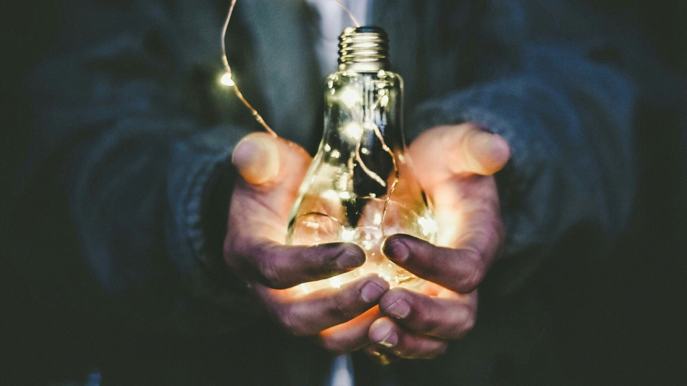 Zwei hände halten eine Glühbirne, um die eine Lichterkette gewickelt ist, die leuchtet | © Riccardo Annandale, Unsplash
