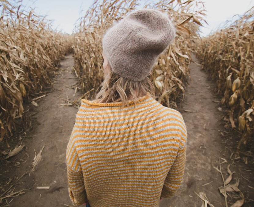 Junge Frau steht in einem Maisfeld vor einer Weggabelung | © Unsplash, Burst