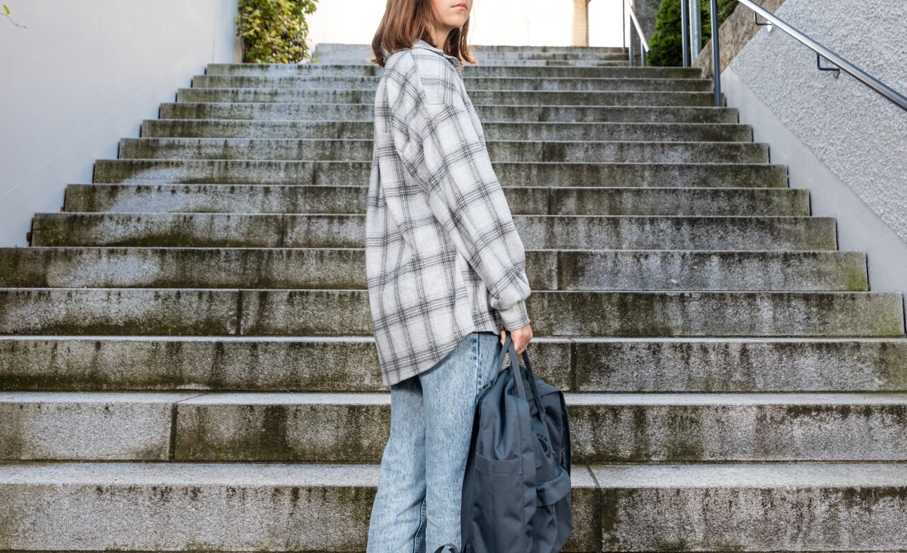 Jugendliche versucht, ihren Weg zu gehen. Sie steht auf einer Treppe und schaut zurück. | © ask! – Beratungsdienste für Ausbildung und Beruf