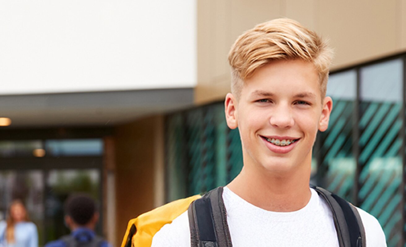 Schüler steht auf dem Schulhof und lacht in die Kamera