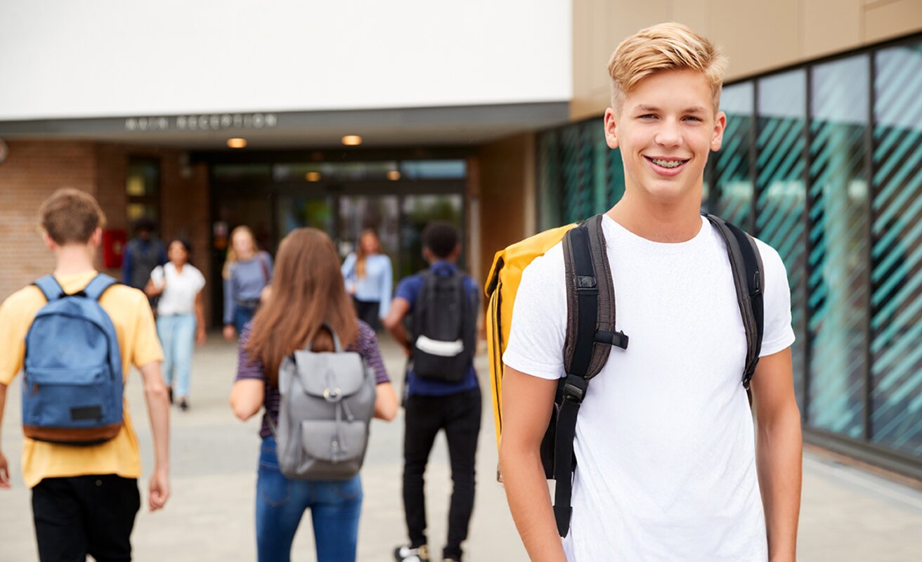 Schüler steht auf dem Schulhof und lacht in die Kamera