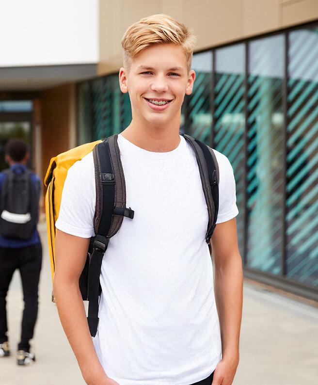 Schüler steht auf dem Schulhof und lacht in die Kamera